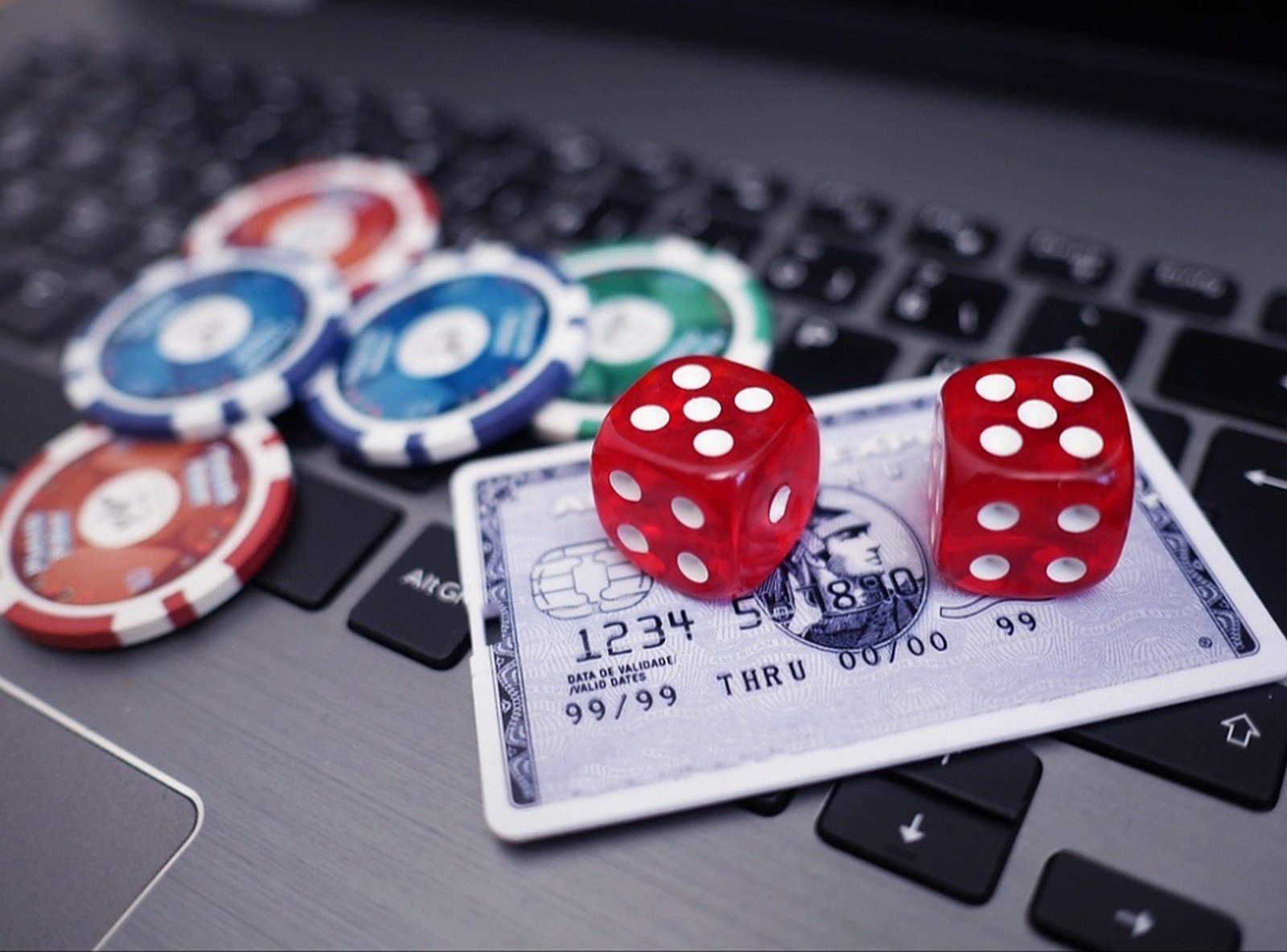 Dice and casino chips on a credit card, resting on a laptop keyboard